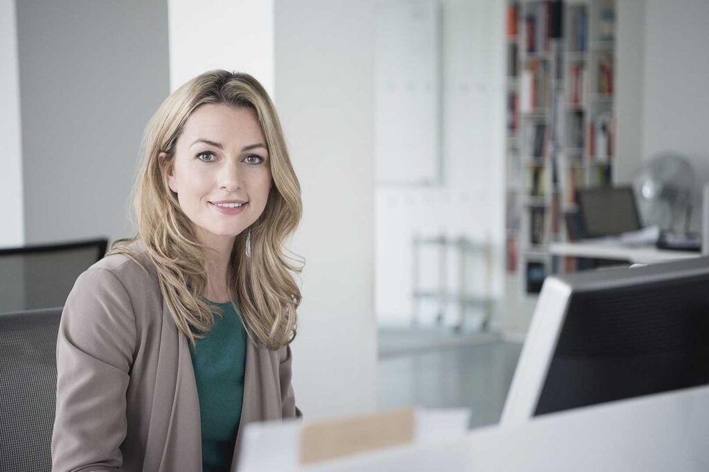 Business woman sitting at desk with a computer smiling towards camera.