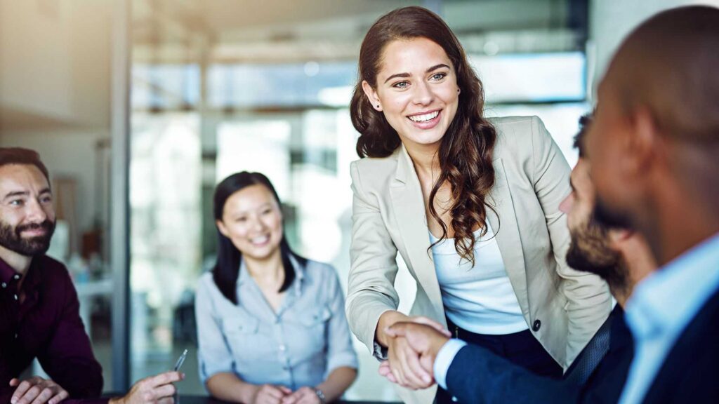 People in business attire and a woman is shaking hands with a man.